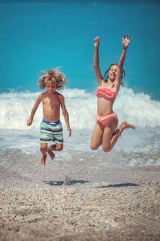 Brother and sister are playing and having fun in the shore on the beach during the hot summer vacation day. They are enjoying and jumping on the beach.