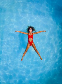 Top view of a beautiful smiling happyyoung woman enjoying in the water of the pool. She is swimming in clear blue water and smiling.