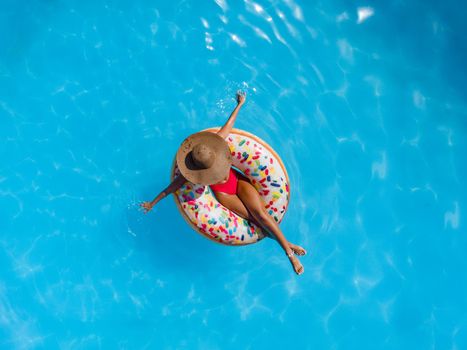 Top view of a beautiful young woman in swimming pool swims on inflatable ring donut and has fun on vacation.