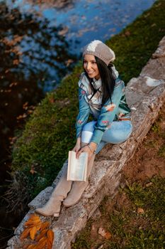 Top view of beautiful young woman enjoying in autumn colors sunny forest looking away and holding a book in her hand.  