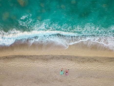 Aerial view of the amazing idyllic beach with two lonely people near waved sea.