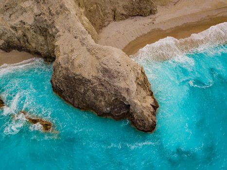 Aerial views of the turquoise sea water with wild seashore and waves reaching sandy beach and steeply rocks on a sunny day. 