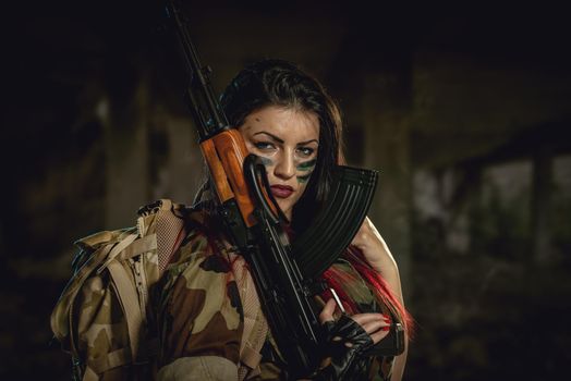 Attractive dark-haired girl in camouflage shirt hold machine gun leaning on the shoulder and with a dangerous expression on her face looking at the camera.