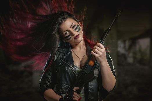 Young attractive military woman with face paint in war paint holding rifle and looking at camera.