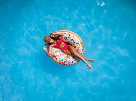 Top view of a beautiful young woman in swimming pool swims on inflatable ring donut and has fun on vacation.