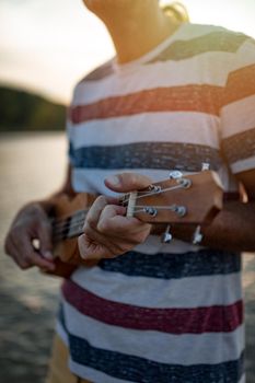 Ukulele in the hands of a young musician. Sunset over water.