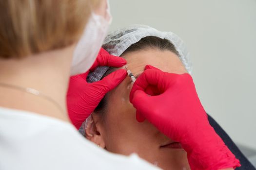 Attractive young woman is getting rejuvenating facial injections. The expert beautician is filling female wrinkles by hyaluronic acid