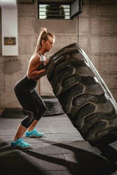 Young muscular woman flipping a tire on cross fit training at the gym.