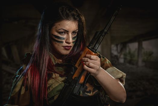 Attractive dark-haired girl in camouflage shirt hold machine gun leaning on the shoulder and with a dangerous expression on her face looking at the camera.