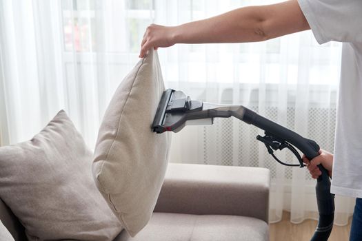 Young housewife Cleaning the Sofa with Vacuum Cleaner in living room