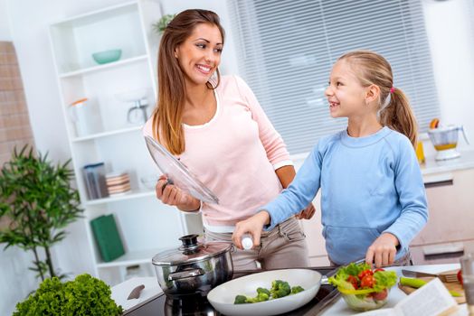 Young beautiful mother and her cute daughter cooking healthy meal in the kitchen.