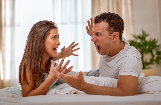 Angry couple is having an argument  in bed. They are shouting at each other.