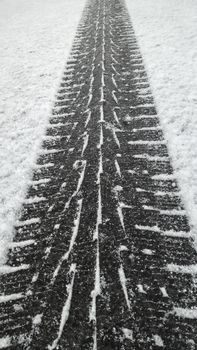 Close up black winter tire tread footprint on white snow of road surface, high angle view, diminishing perspective