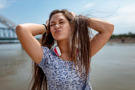 A beautiful cheerful girl pouting, making face and having fun with your hair in the open and enjoying on the city rivershore on a beautiful summer day.