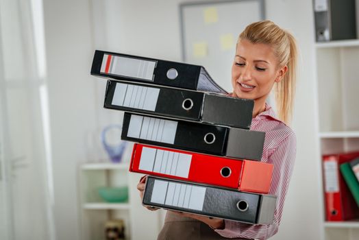 Young business woman wearing a stack of binders in the hands and keep them not to fall.