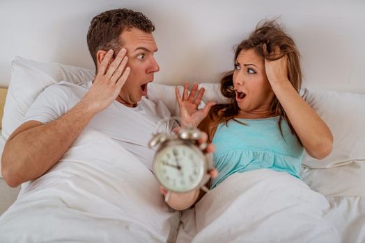Young couple in bed awaken to the ringing of the alarm clock. They are late in the morning.