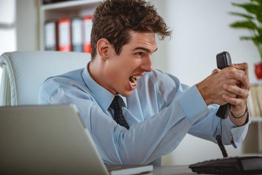 Executive businessman holding an earphone, surprised by bad news he just heard. He is yelling at the phone.