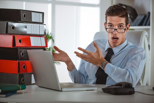 Ayoung businessman working at laptop, looking at documents and accounts and persuades someone in his opinion.