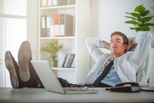 Overworked, tired young businessman sleeping at his desk in office, in front of computer.