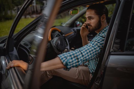 Young confident businessman holding smartphone in his hand and is talking, before he is going to drive.