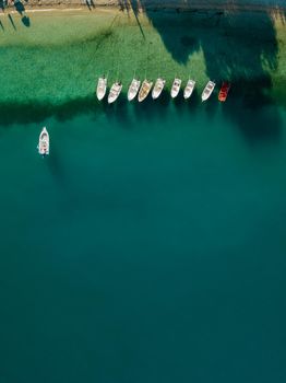 Aerial view of colorful tied boats near Mediterranean seashore. Beautiful summer seascape with boats, clear azure water at sunrise. Top view from flying drone.
