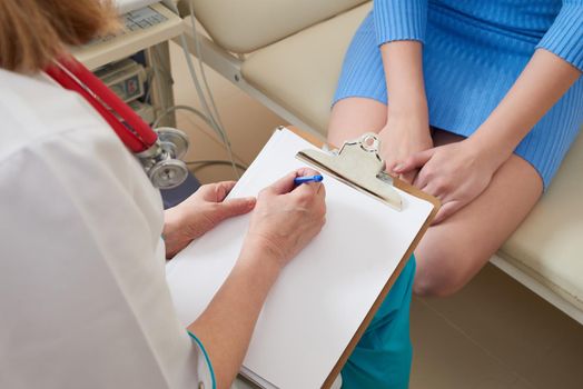 Doctor and patient sit and talk, writing on clipboard