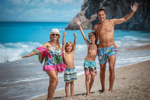 Young family with two sons are posing on the sea beach in summer day and looking at camera.