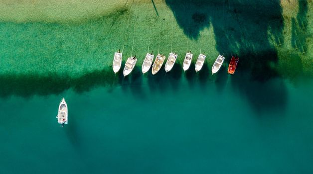 Aerial view of colorful tied boats near Mediterranean seashore. Beautiful summer seascape with boats, clear azure water at sunrise. Top view from flying drone.