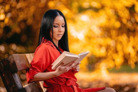 Beautiful young woman enjoying in autumn colors sunny forest reading a book in her hand.  