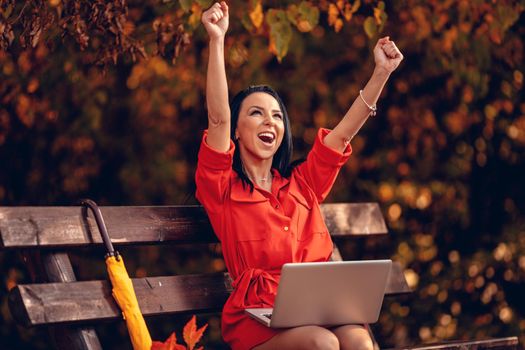 Euphoric young woman entrepreneur celebrating business success reading good news on laptop in the park.