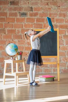 Cute little girl in school uniform posing next to school board with book in her hands, back to school concept