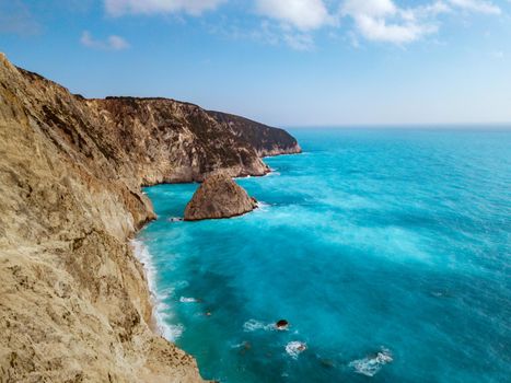 Aerial views of the turquoise sea water with wild seashore and waves reaching steeply rocks on a sunny day.