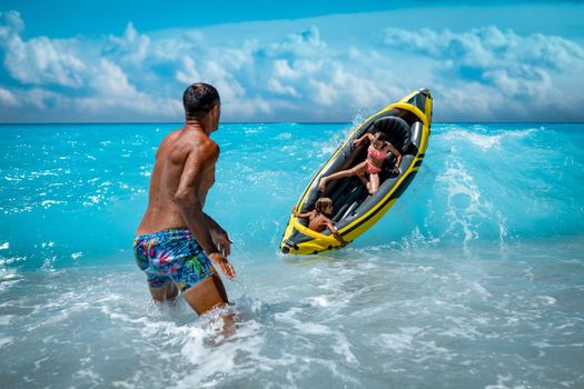 Happy family is enjoying floating in yellow kayak at tropical ocean water during summer vacation. The father is guarding children who are driving in a rubber boat and waves are splashing them.