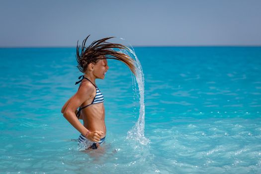 Joyful little girl flips her long hair out of sea and splashes water high in the air.