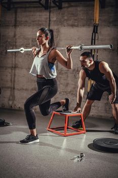 Young woman doing squat exercise at the gym with a personal trainer.