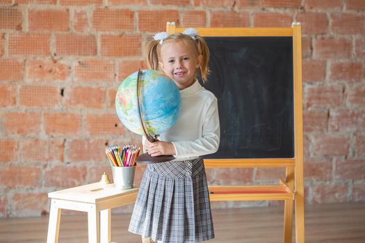 Portrait of caucasian schoolgirl standing in front of chalkboard with globe in her hands, back to school concept