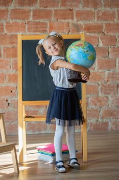 Cute little girl in school uniform posing next to school board with book in her hands, back to school concept