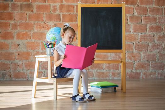 Portrait of caucasian schoolgirl reading a book in front of chalkboard, back to school concept