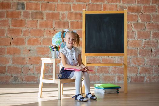 Portrait of caucasian school kindergarten girl sitting in front of blackboard with a book, back to school concept