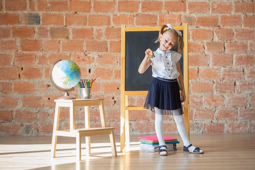 Portrait of caucasian schoolgirl or kindergarten girl smiling in front of blackboard with a bell in her hands, back to school concept