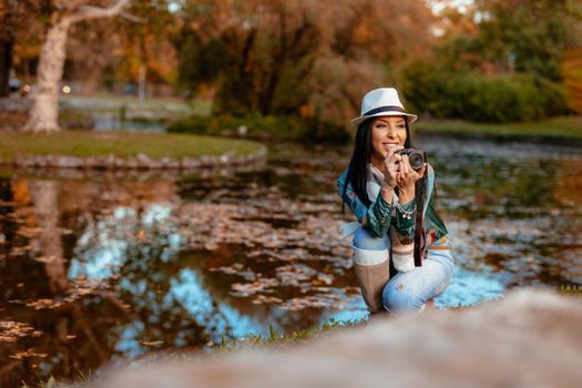 Happy woman photographer holding professional digital camera and taking photo near the lake in autumn park.  