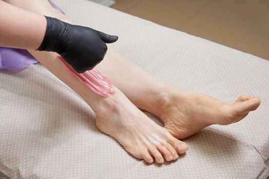 Cosmetologist beautician waxing female legs in the spa center beauty salon cosmetology concept