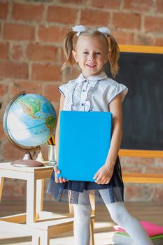 Portrait of caucasian schoolgirl standing in front of chalkboard with book in her hands, back to school concept