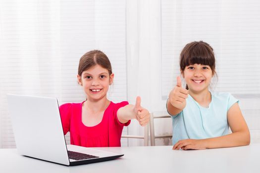 Two little girls using laptop and showing thumbs up