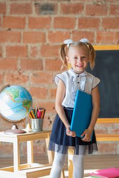 Portrait of caucasian schoolgirl standing in front of chalkboard with book in her hands, back to school concept
