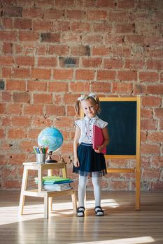 Portrait of caucasian schoolgirl standing in front of chalkboard with book in her hands, back to school concept