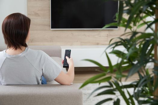 Woman with TV remote control relaxing on sofa in loft apartment