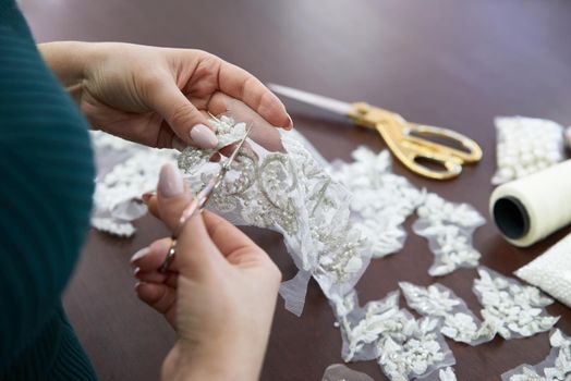 selective focus of seamstress sitting at table, sewing machine and cutting lace with scissors in sewing studio