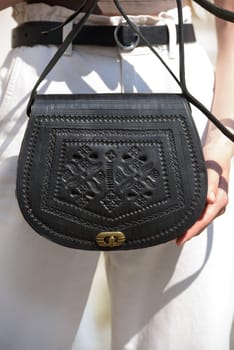 small black women's leather bag with a carved pattern. street photo