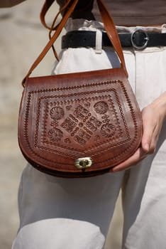 small brown women's leather bag with a carved pattern. street photo